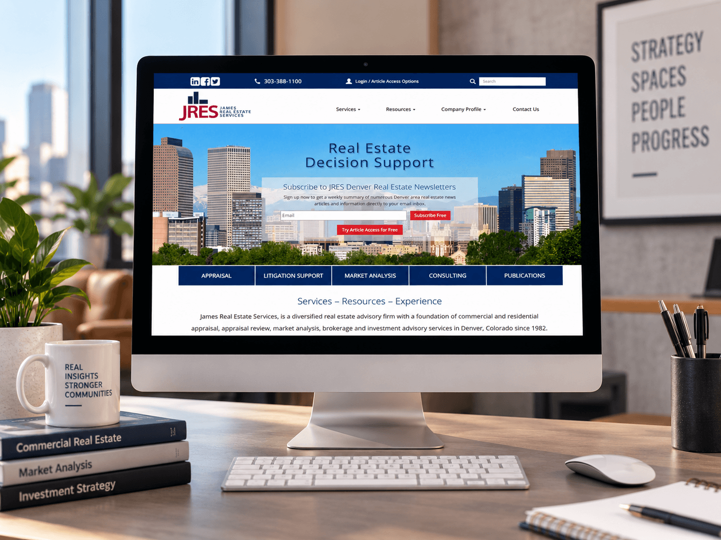 James Real Estate Services website displayed on a desktop monitor in a polished modern office with real estate books, plants, a keyboard, and desk accessories.