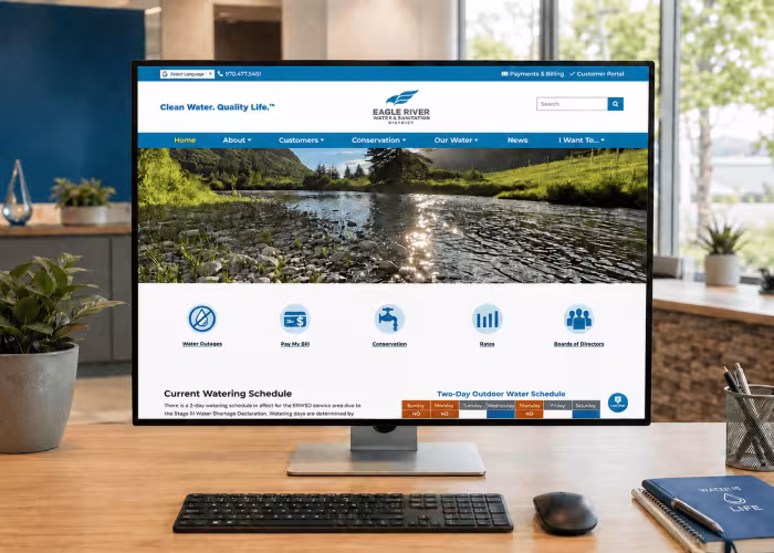 Eagle River Water & Sanitation District website displayed on a desktop monitor in a modern office workspace with plants, a keyboard, mouse, and water-themed desk accessories.